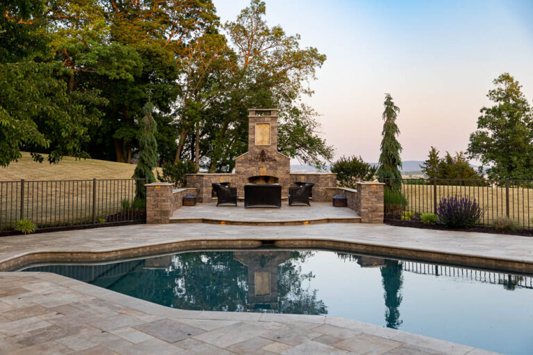 outdoor fireplace with comfy deck chairs beside a pool