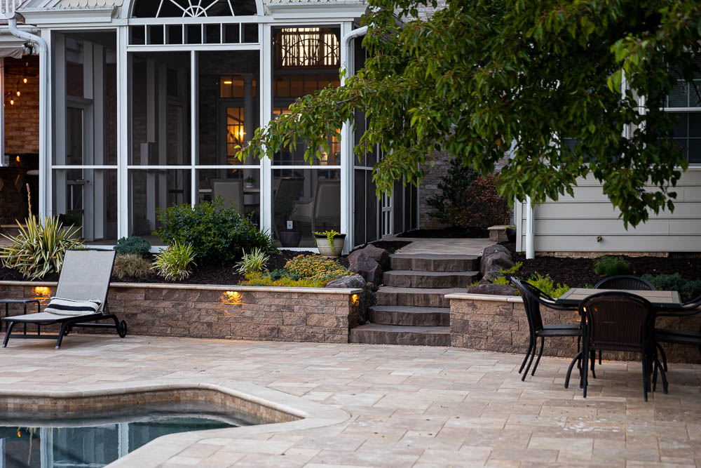 paver patio around a pool with a retaining wall with lights