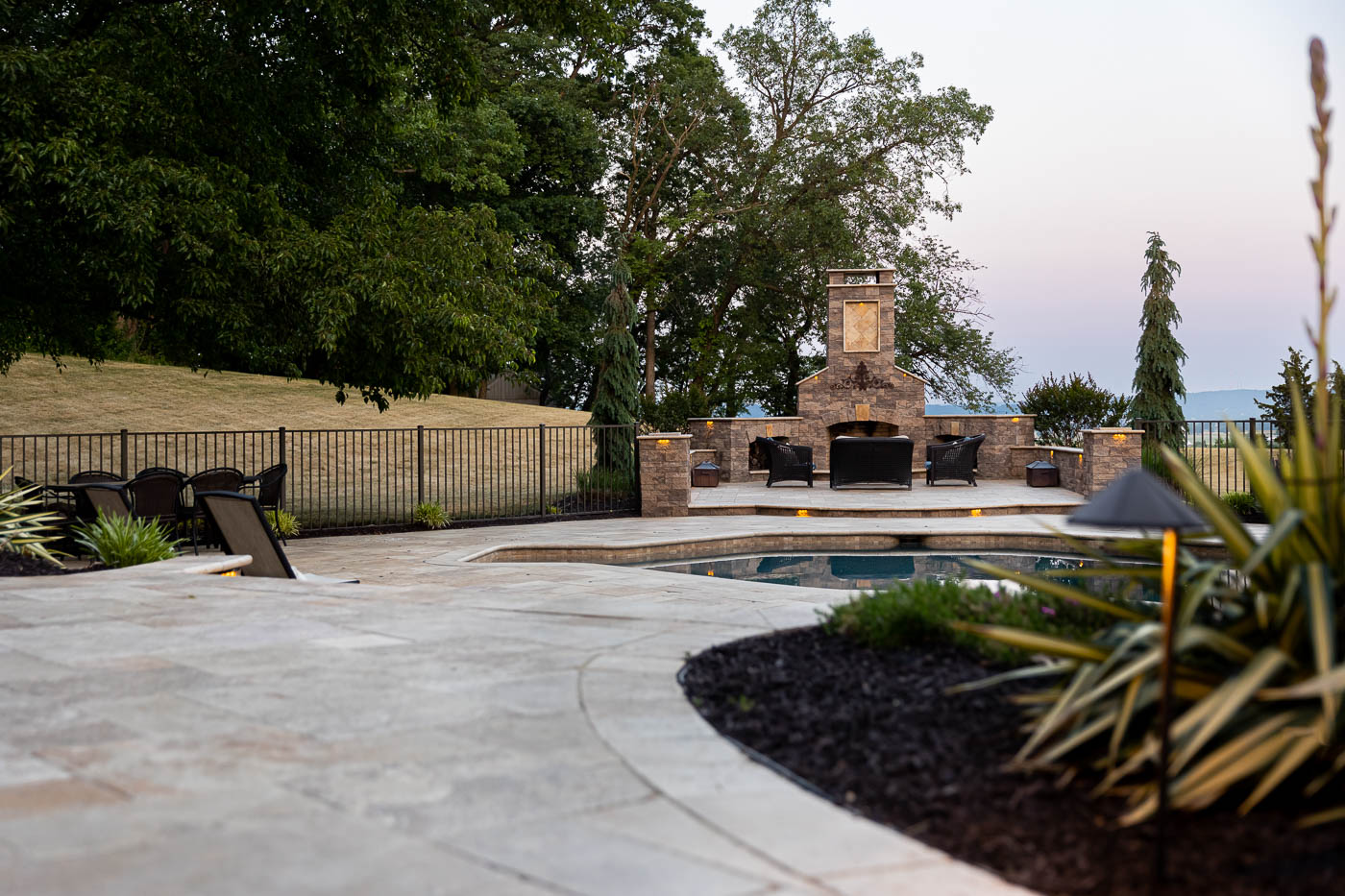 outdoor fireplace with comfy deck chairs beside a pool